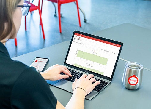 A person works at a computer, while a Fastly-branded cup sits off to the side.